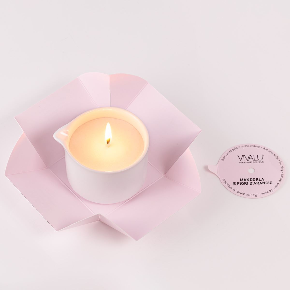 Candela da massaggio Vivalù accesa, con fiamma delicata e confezione rosa aperta.
