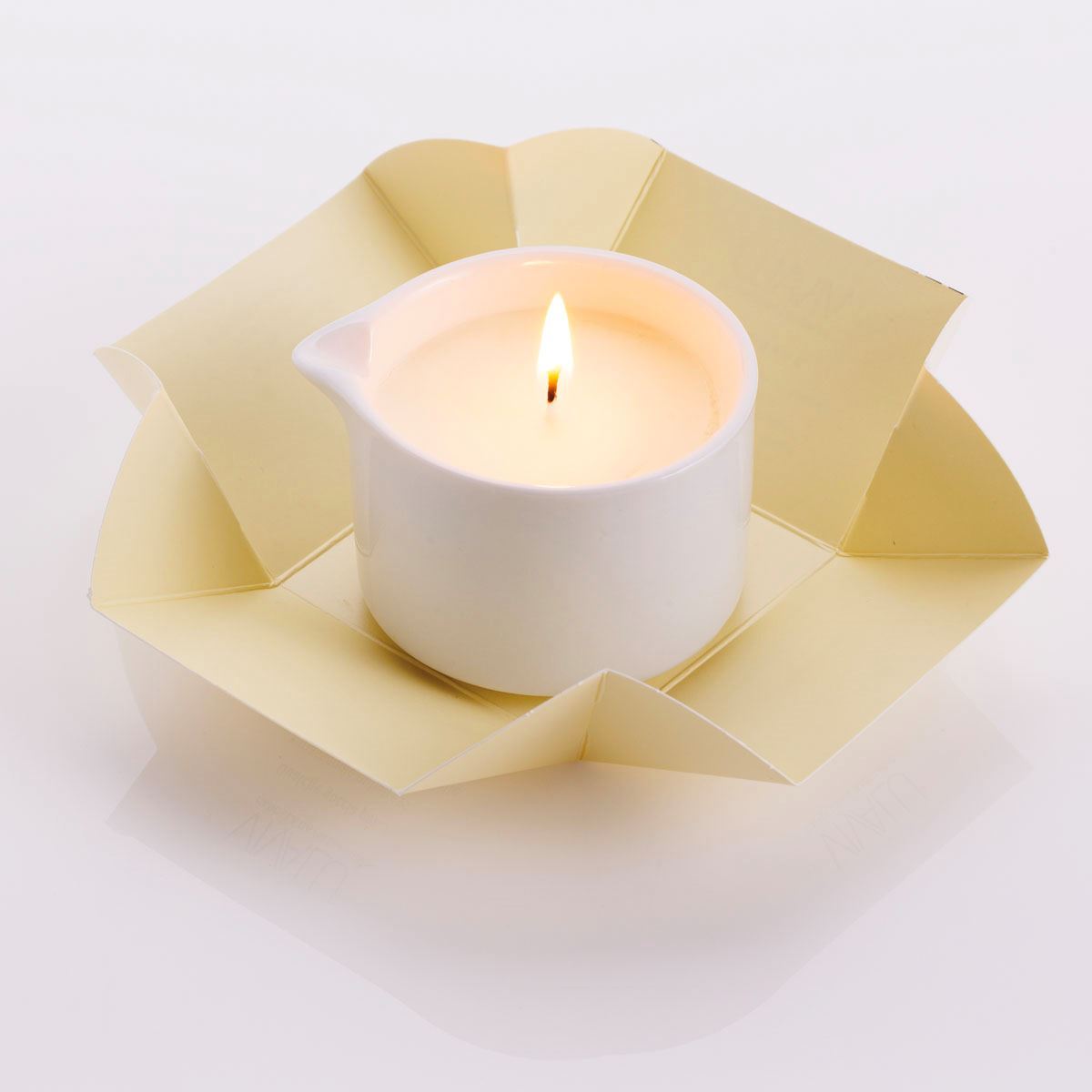 Candela da massaggio alla vaniglia Vivalu accesa, con confezione aperta color crema e fiamma ardente.